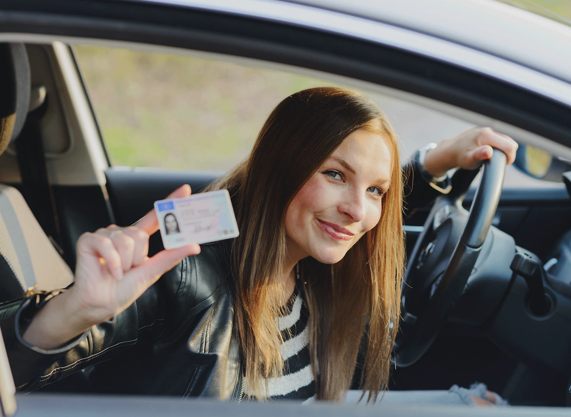 Primer pla d'una conductora asseguda al volant que mostra somrient el seu permís de conduïr.